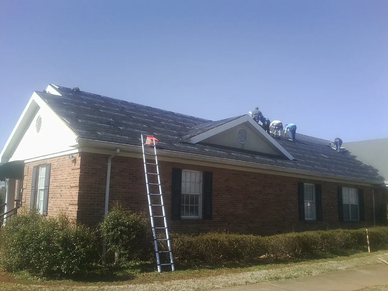 Crew tearing shingles off a brick ranch roof with a ladder set — Emergency Roof Repair work by our crew in Mill Run