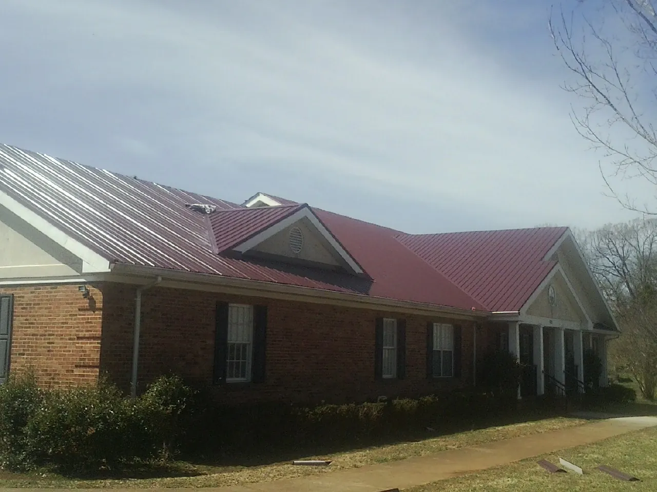 Red metal roof with gabled entries on a long brick building, from a Hail Damage Roof Repair job in Mill Run