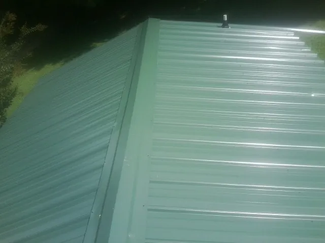 New green metal panels meeting at the ridge of a roof — Flat Roof Repair work by our crew in Mill Run