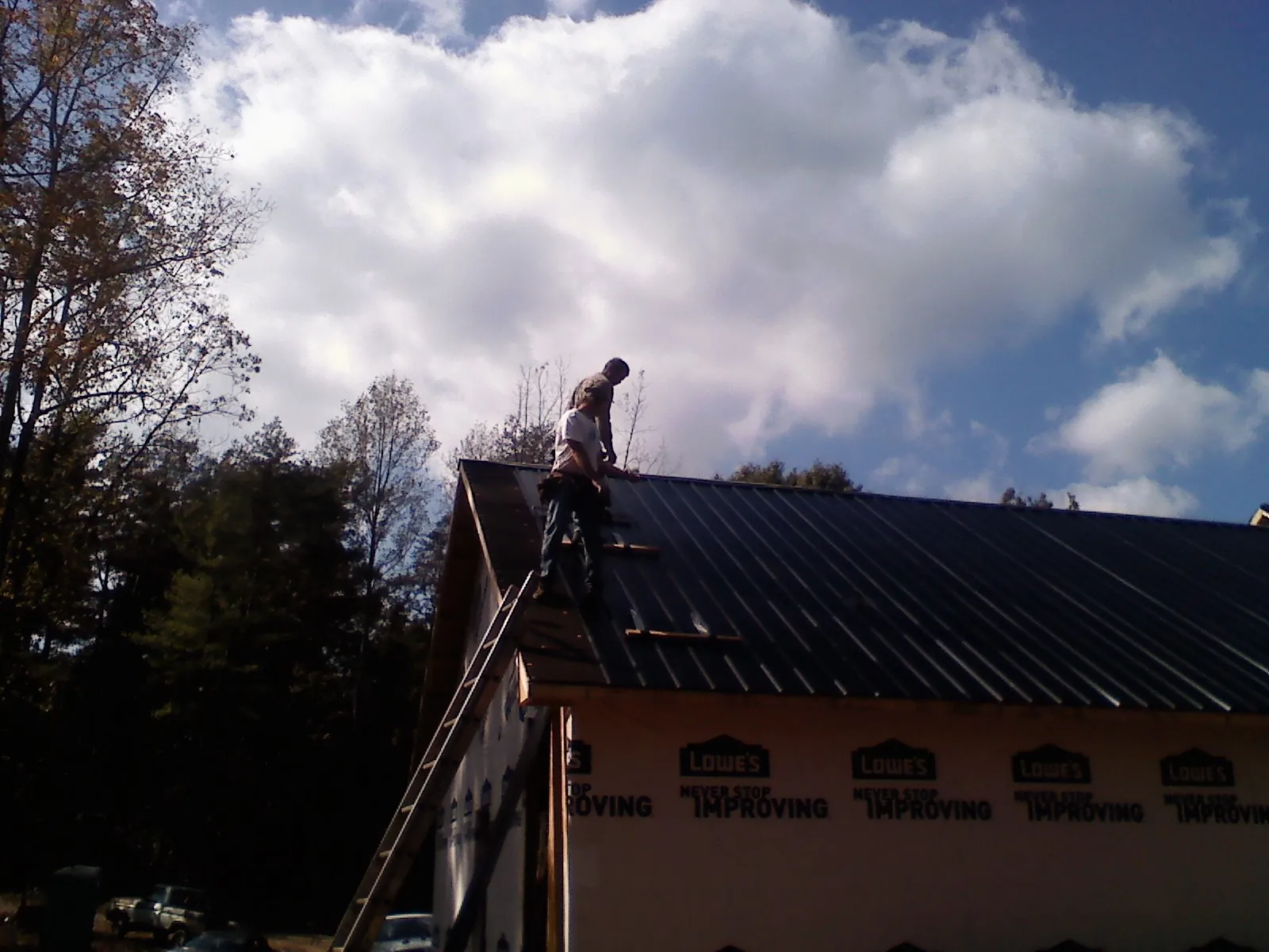 Roofer fastening dark metal panels high against a cloudy sky, from a Roof Inspection job in Mill Run