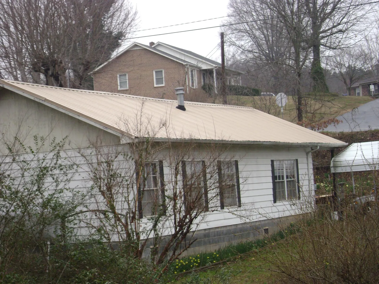 Tan metal roof on a white sided house set into a hillside — Commercial Roofing by Roofing Brothers in Mill Run